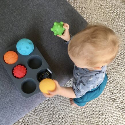 Ein Baby räumt Bälle in Muffinformen
