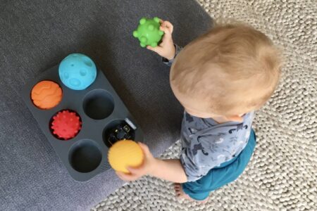 Ein Baby räumt Bälle in Muffinformen