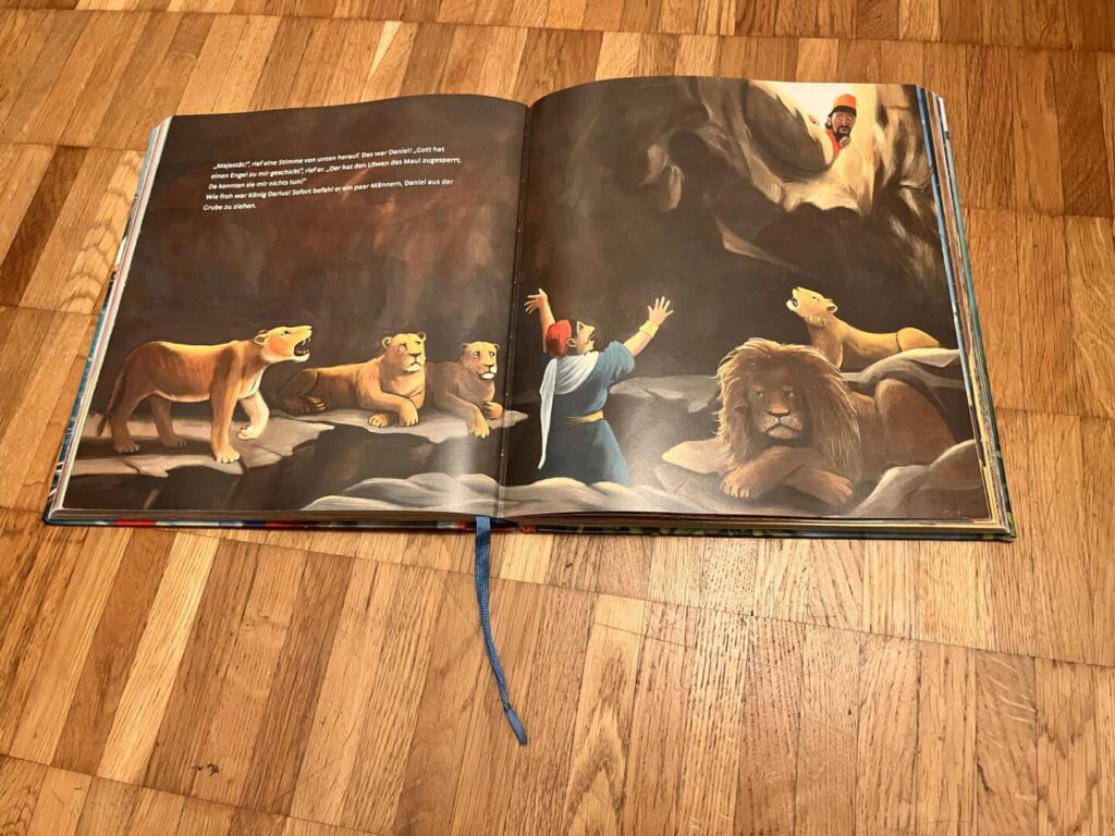 Aufgeschlagene Doppelseite mit der Geschichte von Daniel in der Löwengrube – dramatische Illustration mit Löwen und Engel