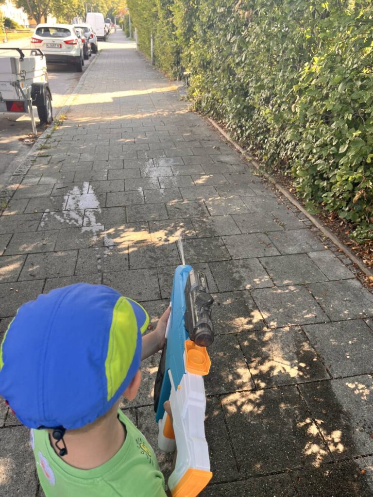 Kind zielt mit Wasserpistole auf Kreide-Feuer auf dem Gehweg – Wasserspiele bei Hitze