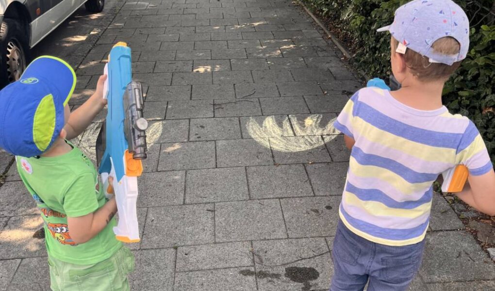 Zwei Kinder löschen mit Wasserpistolen ein aufgemaltes Kreide-Feuer – Wasserspiele ab 3 Jahren