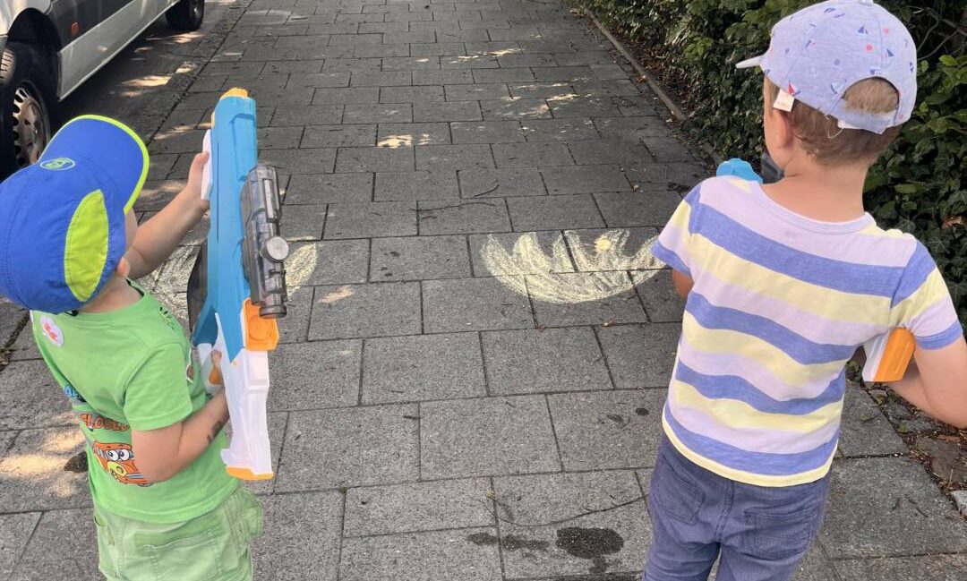 Zwei Kinder löschen mit Wasserpistolen ein aufgemaltes Kreide-Feuer – Wasserspiele ab 3 Jahren