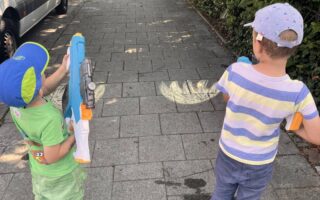 Zwei Kinder löschen mit Wasserpistolen ein aufgemaltes Kreide-Feuer – Wasserspiele ab 3 Jahren