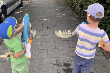 Zwei Kinder löschen mit Wasserpistolen ein aufgemaltes Kreide-Feuer – Wasserspiele ab 3 Jahren