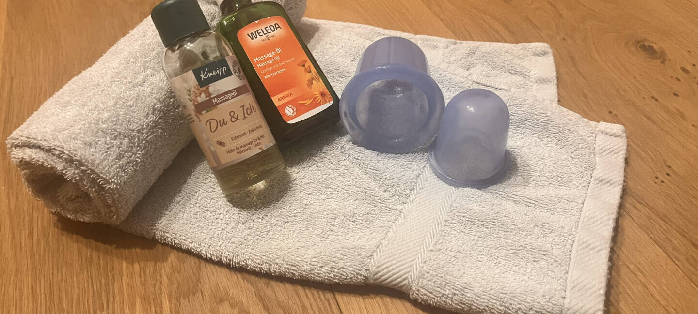 Silikon-Cups und Massageöl auf einem Handtuch – Material zum Schröpfen zuhause
